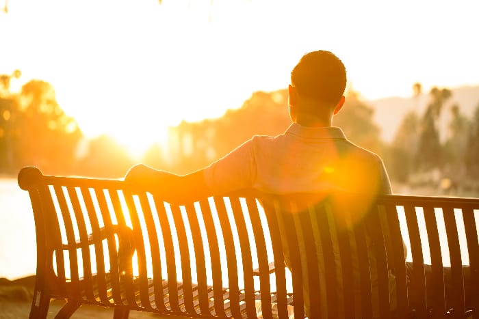 Man reflecting on his journey, sitting on a bench during sunset, representing the hope found in addiction counseling in Riverside CA.